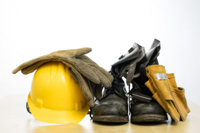 Protective helmet and work boots on a wooden table. Safety and health protection accessories for construction workers. White isolated background.